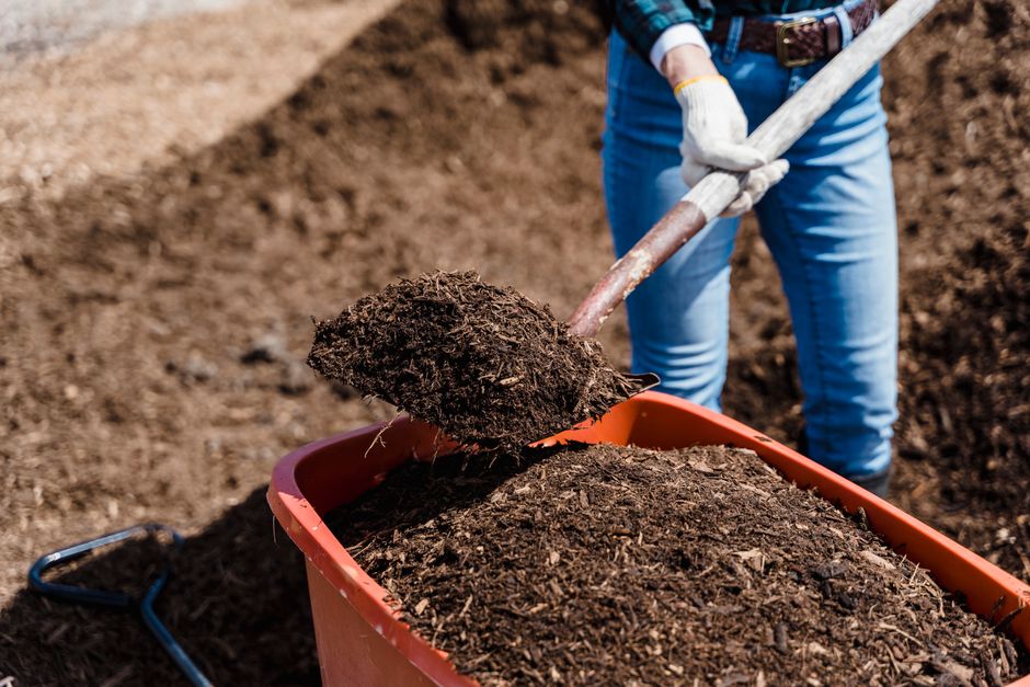 A person shovels compost into a red container, preparing soil for gardening.